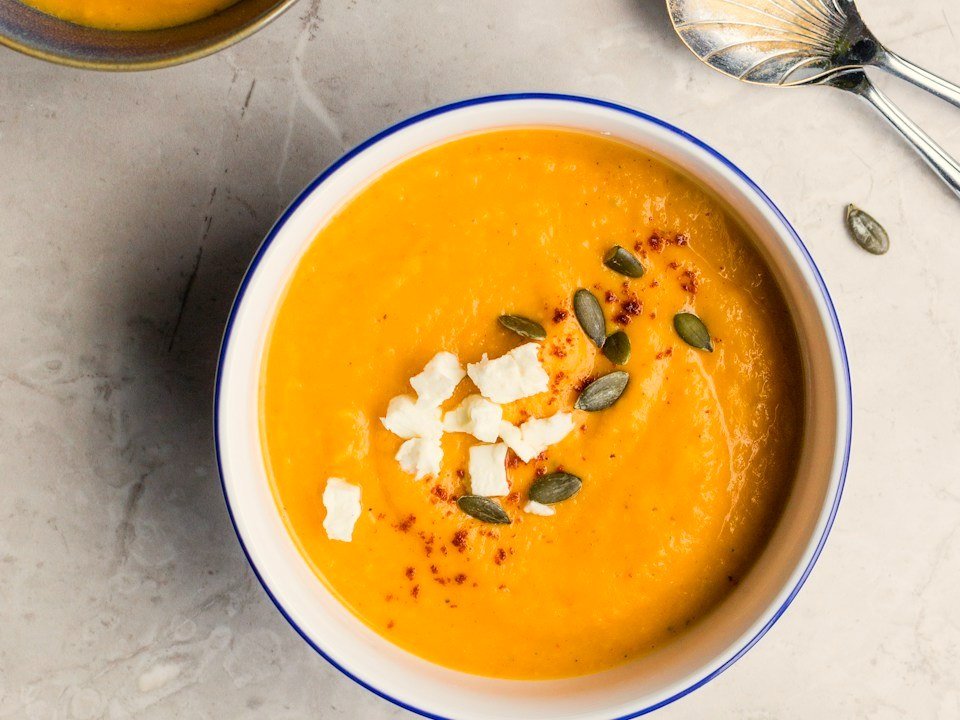 Concept photo: creamy butternut squash soup in a white bowl with pepitas and cheese